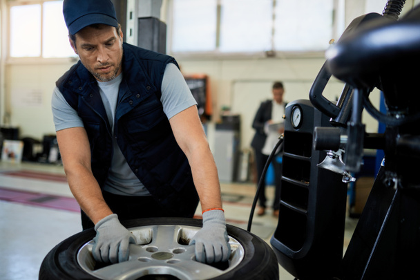 Mid adult mechanic working with car tire in auto repair shop.  - Foto, immagini