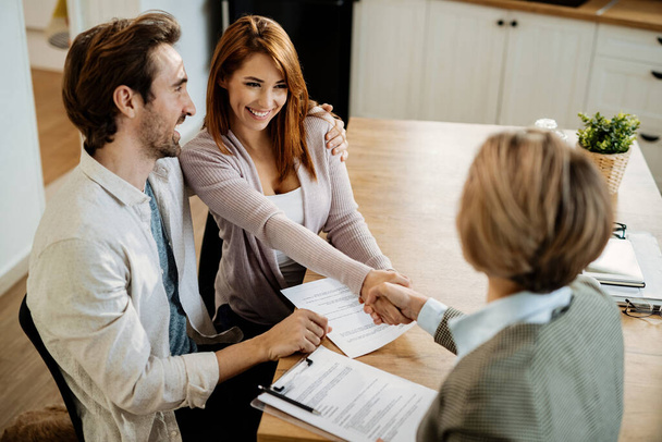Young happy couple shaking hands with insurance agent while having a meeting at home. Focus is on young woman.  - Foto, Imagem
