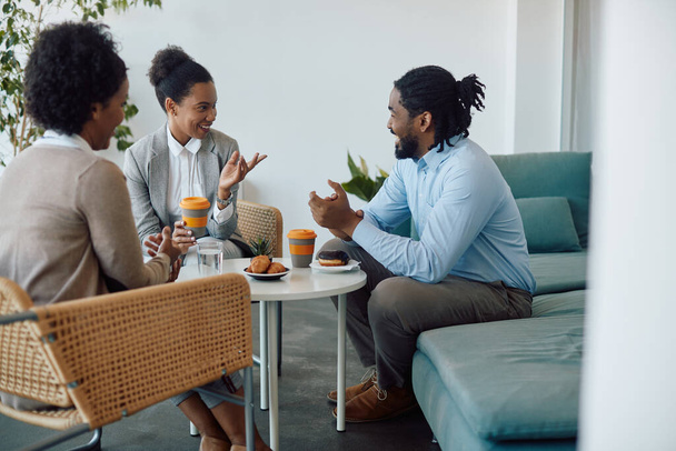 Happy black entrepreneurs enjoying while communicating during coffee break at work. - Foto, afbeelding