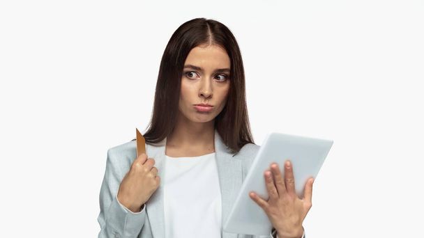 pensive businesswoman in grey blazer holding credit card and digital tablet isolated on white - 写真・画像