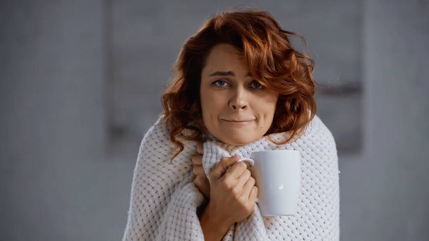 redhead and sick woman covered in blanket holding cup with hot beverage - Foto, immagini