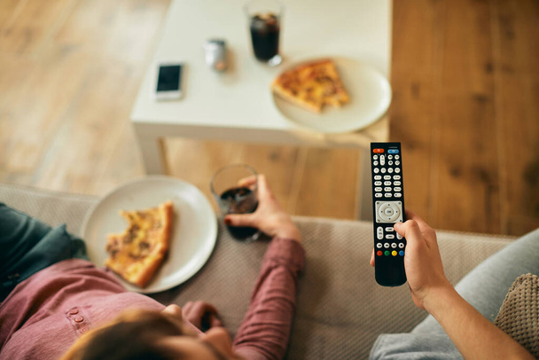 Close-up of couple changing channels on TV while eating pizza at home. - Photo, Image