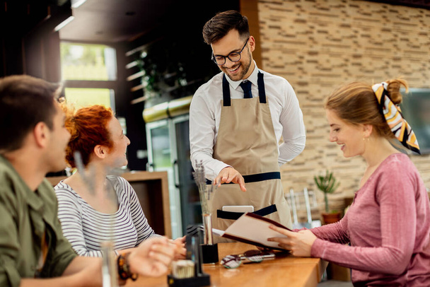 Счастливый официант развлекается, общаясь со своими гостями и принимая у них заказы в кафе,  - Фото, изображение
