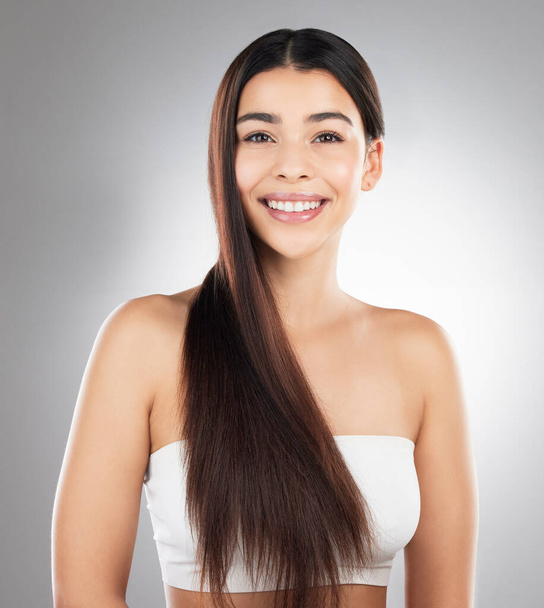 Studio portrait of a beautiful young woman showing off her long silky hair against a grey background. - Foto, immagini