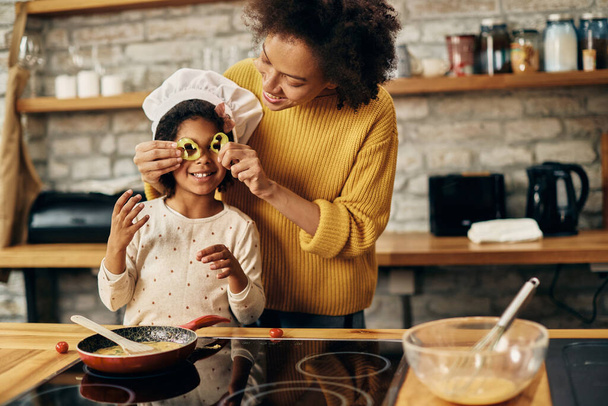 Happy black little girl and her mother having fun with food while cooking together in the kitchen.  - Foto, Bild