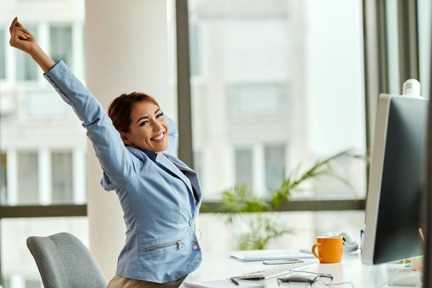 Happy businesswoman stretching while working on desktop PC in the office.  - Foto, Imagen