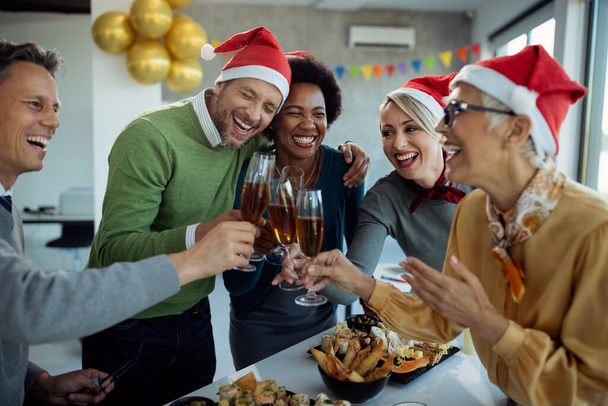 Fröhliche Geschäftskollegen amüsieren sich und stoßen mit Champagner auf die Neujahrsparty im Büro an.  - Foto, Bild