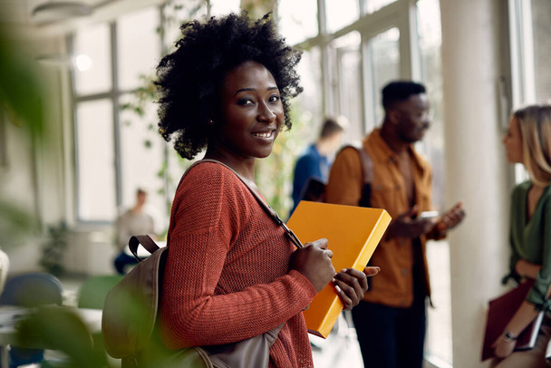Happy African American university student standing in a hallway and looking at camera.  - 写真・画像