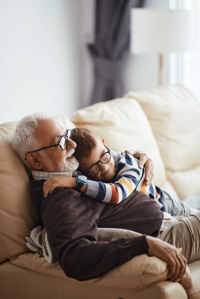 Щасливий маленький хлопчик обіймає свого діда, проводячи час разом вдома
.  - Фото, зображення