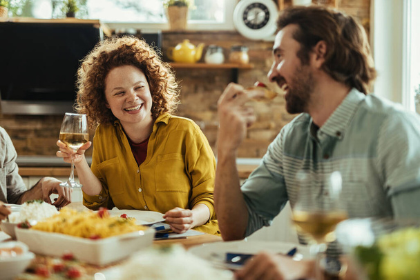 Young cheerful woman and her boyfriend communicating while eating and drinking wine at dining table.  - Foto, Imagen