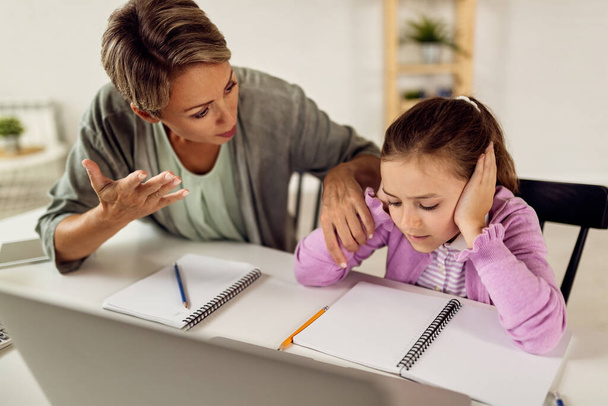 Little girl covering her ears and ignoring mother who is trying help her with a homework.  - Foto, afbeelding