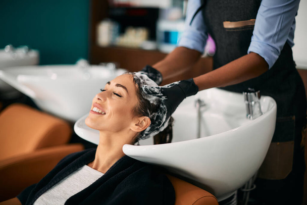 Χαμογελαστή γυναίκα που κάνει μασάζ στο κεφάλι ενώ πλένει τα μαλλιά στο κομμωτήριο.  - Φωτογραφία, εικόνα