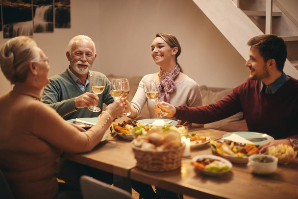 Щасливі сімейні тости з вином, збираючись навколо обіднього столу вдома
. - Фото, зображення