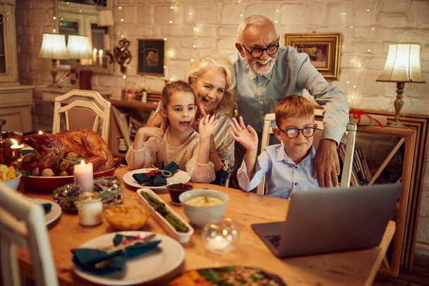 Happy children and their grandparents waving while greeting someone during video call on Thanksgiving. - Foto, Imagem