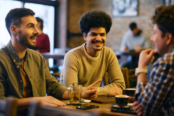 Multiracial group of young men talking while gathering in a cafe. Focus is on Muslim man.  - Photo, image