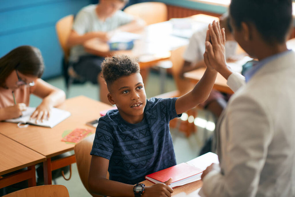 Black elementary student giving high-five to his teacher during a class at school. - Fotó, kép