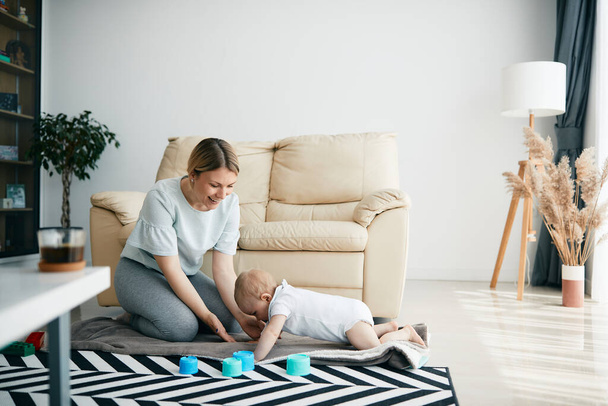 Молода мати розважається зі своїм маленьким сином, граючи з ним на підлозі у вітальні
. - Фото, зображення