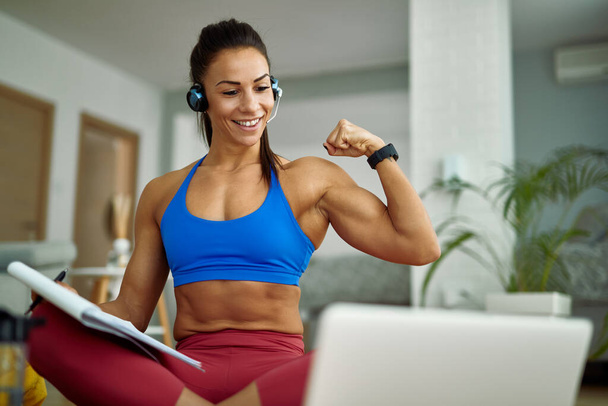Young happy sportswoman flexing her bicep while making video call over laptop at home.  - Φωτογραφία, εικόνα