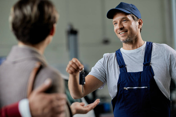 Happy auto repairman handing over cark keys to his customers in a workshop.  - Φωτογραφία, εικόνα