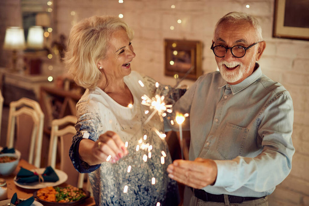 Happy mature couple using sparklers and having fun together on Christmas day at home.  - Valokuva, kuva
