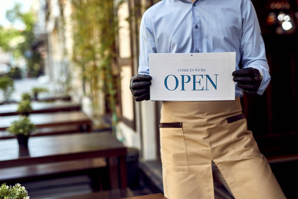Unrecognizable coffee shop owner holding open sign while standing at the doorway.  - 写真・画像