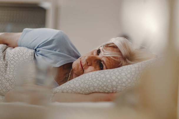 Pensive senior woman lying in the bed and thinking of something.  - Photo, Image