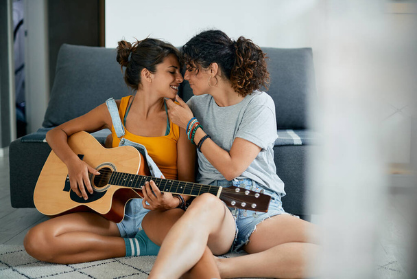 Young lesbian couple in love playing acoustic guitar at home. - Φωτογραφία, εικόνα