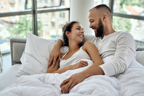 Happy couple communicating while lying embraced on in the bedroom.  - Valokuva, kuva