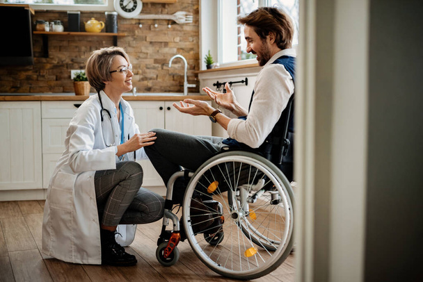 Szczęśliwa kobieta lekarz i jej niepełnosprawny pacjent na wózku inwalidzkim komunikacji podczas wizyty w domu.  - Zdjęcie, obraz