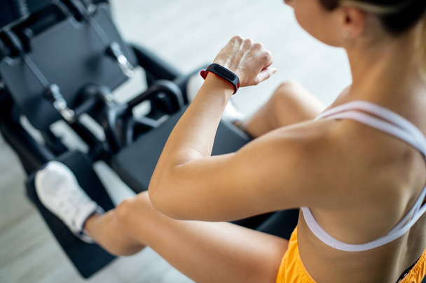 Close-up of sportswoman using fitness tracker while working out on exercise machine in a gym. - Φωτογραφία, εικόνα