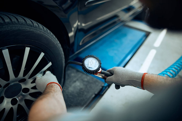 Close-up of mechanic using pressure gauge while examining car tire in a workshop - Foto, Imagen