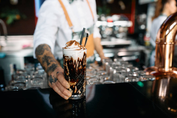 Close-up of barista serving iced coffee in tall glass at bar counter.  - Fotografie, Obrázek