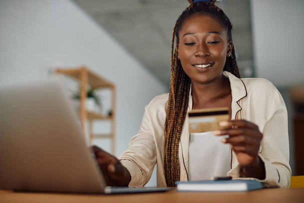 Mladý šťastný černošky žena nakupování on-line při použití notebooku a kreditní karty doma. - Fotografie, Obrázek