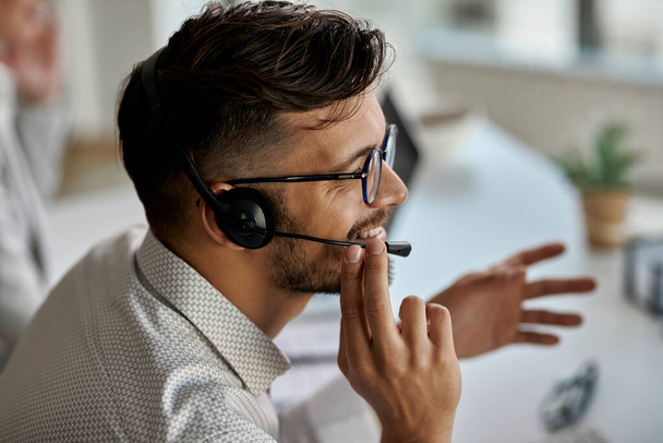 Happy call center agent wearing headset while talking with clients and working in the office.  - Foto, Bild
