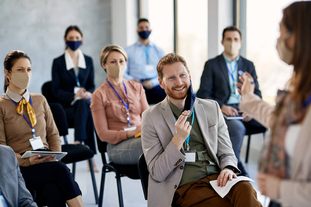 Happy businessman taking off his face mask while communicating with presenter during seminar in conference hall. - Φωτογραφία, εικόνα