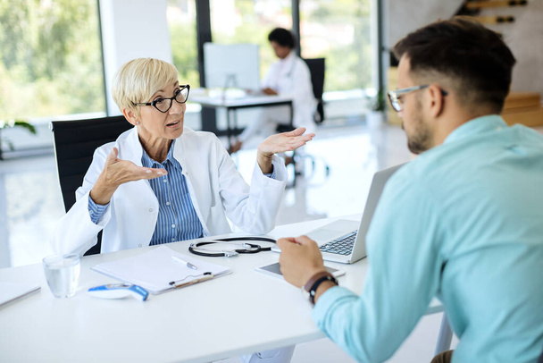 Зрелая женщина-врач общается с пациентом мужского пола, который пришел на медицинский осмотр в клинику.  - Фото, изображение