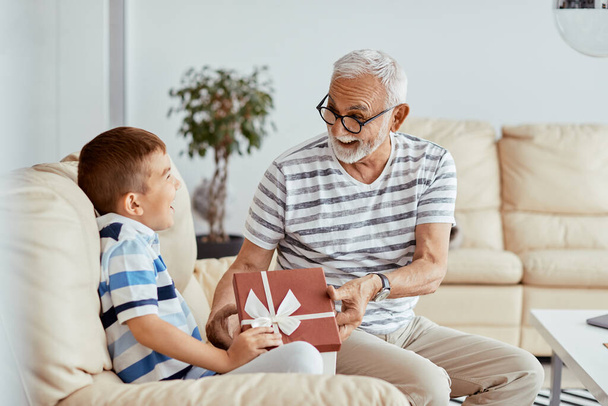 Happy grandfather and grandson having fun while opening gift box at home. - Foto, imagen
