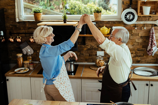 Happy senior couple dancing and having fun together in the kitchen. - Foto, Imagem
