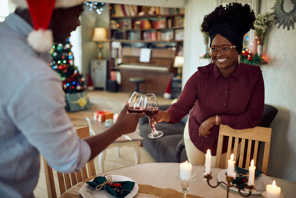 Νεαρό μαύρο ζευγάρι γιορτάζει τα Χριστούγεννα και κάνει πρόποση με κρασί στο σπίτι. Εστίαση στη γυναίκα..  - Φωτογραφία, εικόνα
