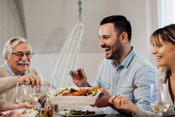 Happy mid adult man having fun while eating with his family at dining table.  - Photo, Image