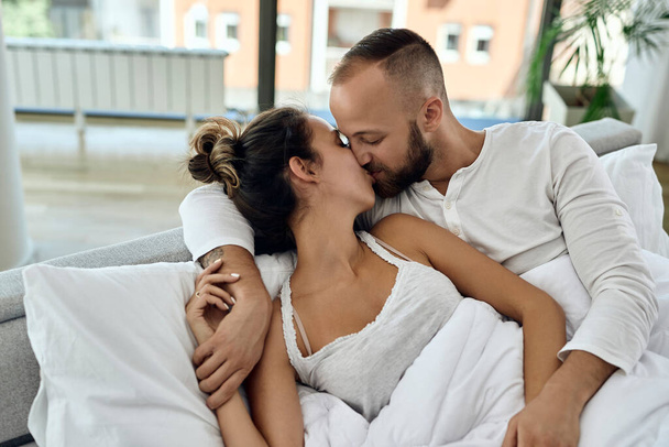 Young couple in love lying embraced on a bed and kissing in the morning.  - Foto, afbeelding