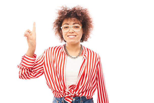 Positive kazakh girl with afro hairstyle points forefinger at copy space isolated on white studio background - Фото, изображение