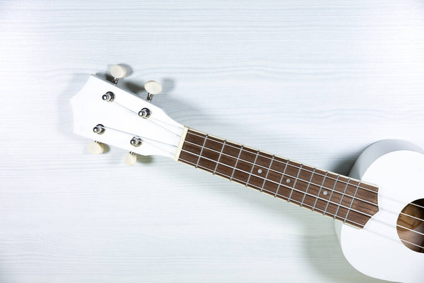 Wit gekleurde houten ukelele gitaar op de witte houten achtergrond. Hawaiiaanse vier snarige gitaar. Muziekinstrument. - Foto, afbeelding