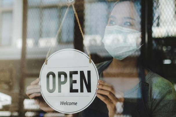 asian waitress staff woman turning open sign board on glass door with bokeh light in cafe coffee shop for lift lockdown, hotel service, cafe restaurant, small business owner, food and drink concept - Fotó, kép