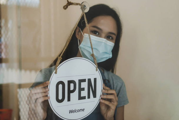 waitress staff wearing protection face mask turning Open sign board reopen after coronavirus quarantine is over in cafe coffee shop ready to service, reopen, cafe restaurant, food and drink concept - Foto, Bild