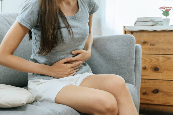 asian young woman suffering stomach ache sitting on couch in living room at home, people painful stomachache, gynecology, menstrual pain , medical and health care concept - Photo, image