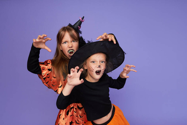 Funny children in carnival costumes of skeleton and witch in honor of Halloween on a purple background. - Fotoğraf, Görsel