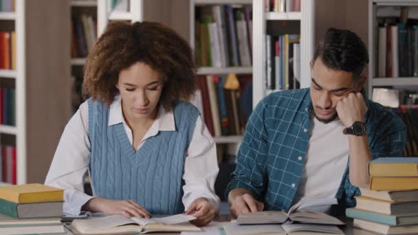 Close-up couple students studying in library preparing for exam working on project read books young girl wakes up sleeping friend funny guy dozing at desk pranks on girlfriend joking laughing smiling - Πλάνα, βίντεο