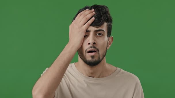 Male portrait of arabic indian disappointed guy upset stressful man stand in green studio cover face with hand outrage puts palm on head shame lost problem feeling exhaustion shows unpleasant emotion - Metraje, vídeo
