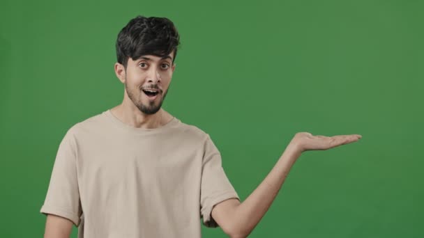 Indischer Mann lächelnd empfehlen leere Fläche über grünem Hintergrund hält Kopierraum auf der Hand Reklamepunkte auf leeren Platz arabischer Kerl mit Attrappe für Promo-Werbung Daumen hoch Finger beste Wahl Zeichen - Filmmaterial, Video